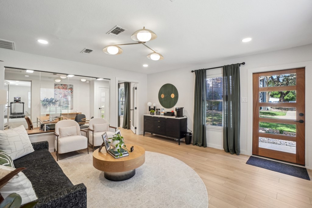 A modern living room with a black sofa, a wooden coffee table, and a large window with green curtains.