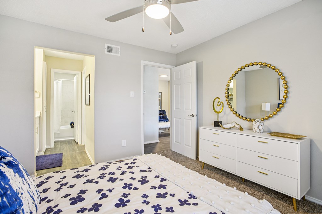 A bedroom with a bed, dresser, mirror and a ceiling fan.