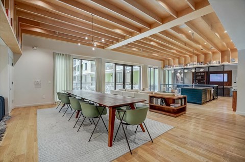 Community dining table with modern chairs beneath dramatic wood ceiling beams.