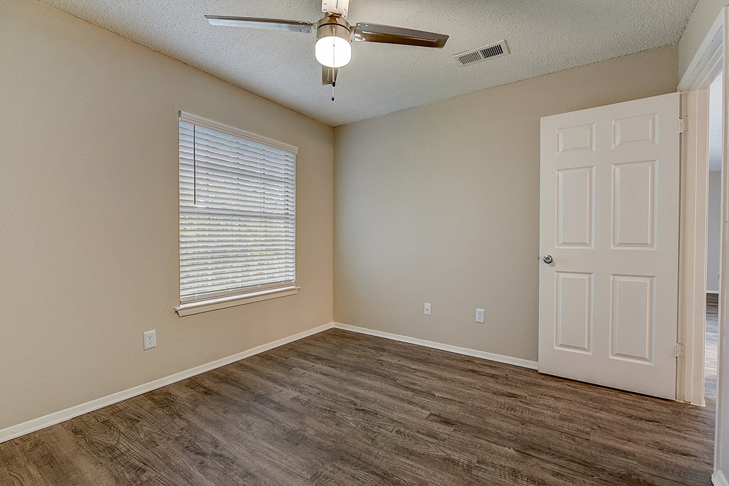 an empty living room with a white door and a ceiling fan