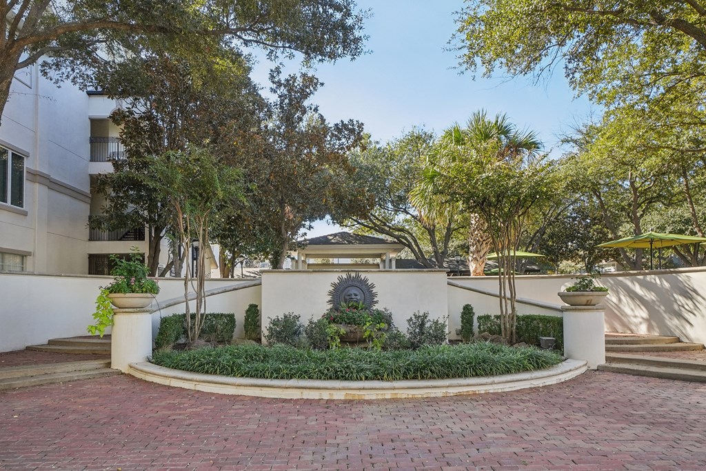 A courtyard with a circular brick walkway and a white wall with a planter in the middle.