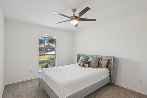 A bedroom with a bed, pillows, and a ceiling fan.