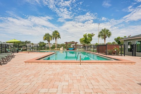 A pool surrounded by a brick patio with trees in the background.
