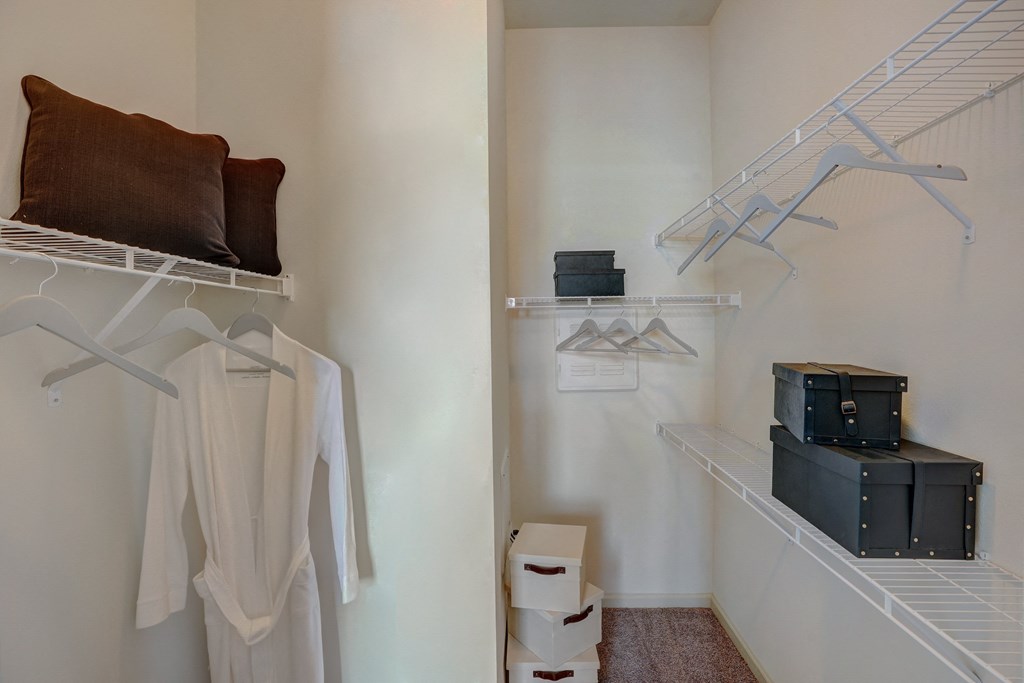a closet with white clothes and boxes on the floor and a white wall with shelves