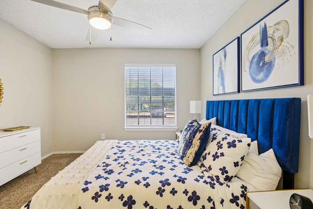 A bedroom with a bed, blue comforter, and two framed pictures on the wall.