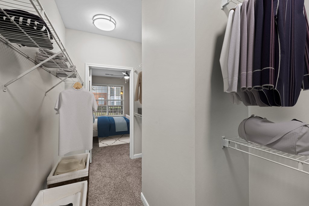 a walk in closet with clothes hanging on the wall and a bedroom in the background