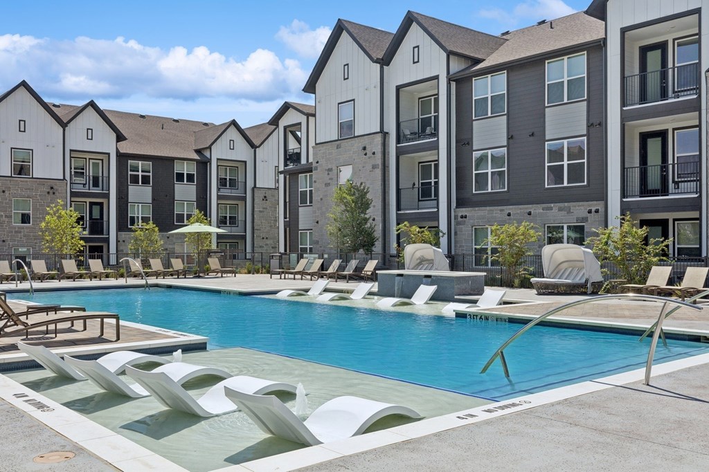 A pool surrounded by lounge chairs and buildings in the background.