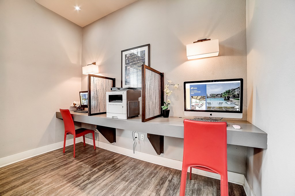 a desk with two computer monitors and two red chairs