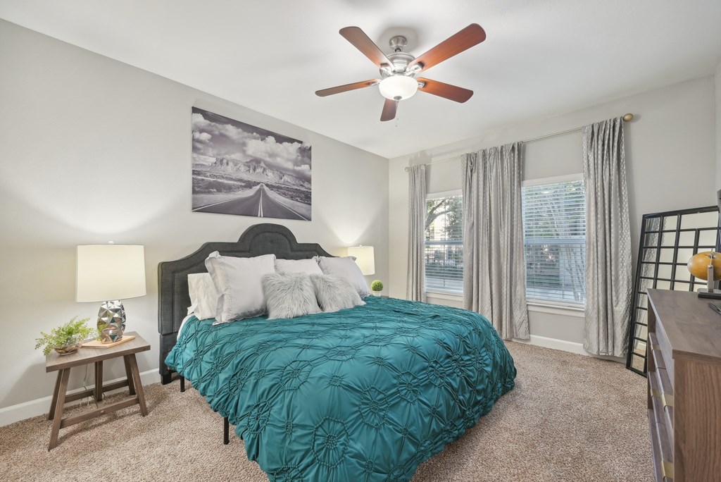 A bedroom with a bed, a ceiling fan, and a painting on the wall.