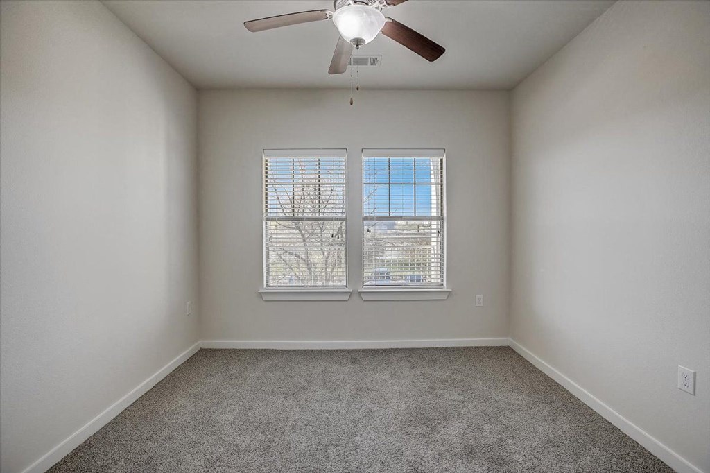 an empty room with a ceiling fan and two windows