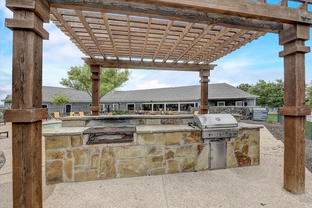 an outdoor kitchen with a stone wall and a pergola