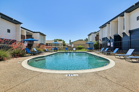 A swimming pool surrounded by lounge chairs in a residential area.
