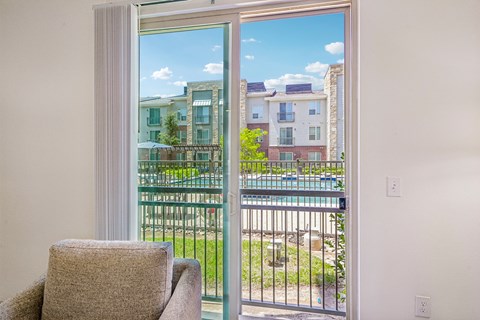 A chair sits in a room with a view of a pool and apartment buildings outside.