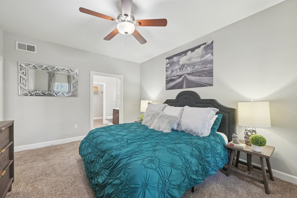 A bedroom with a bed, a ceiling fan, and a small table with a plant on it.
