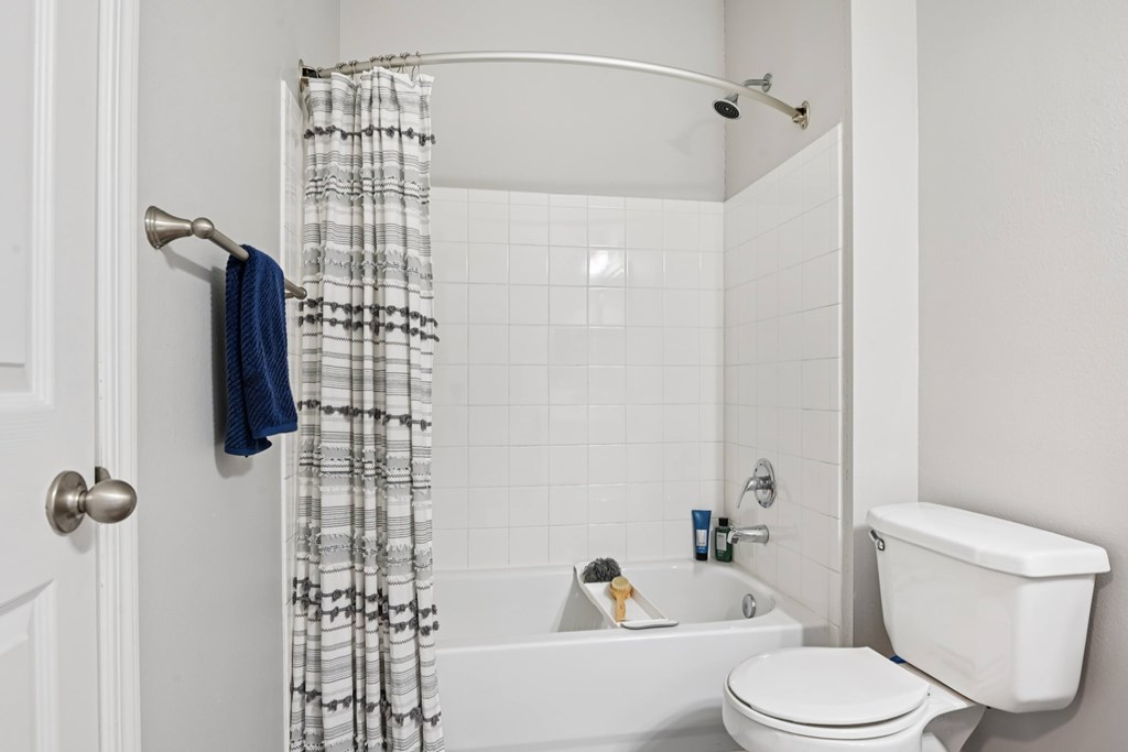 A white bathroom with a white toilet, white tub, and a white shower curtain.