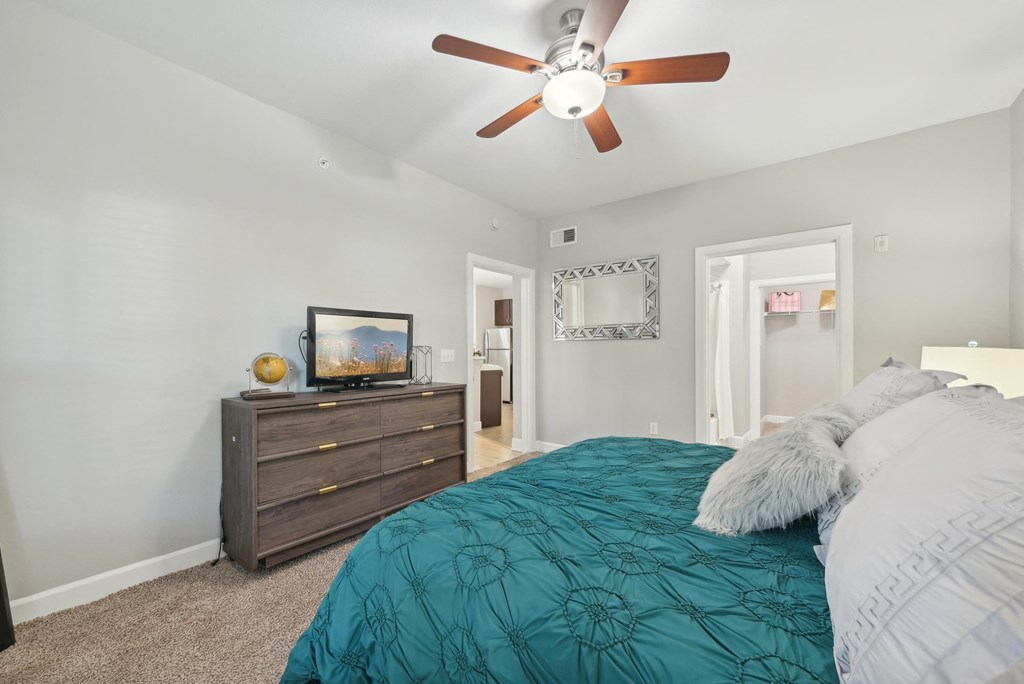 A bedroom with a bed, dresser, and ceiling fan.