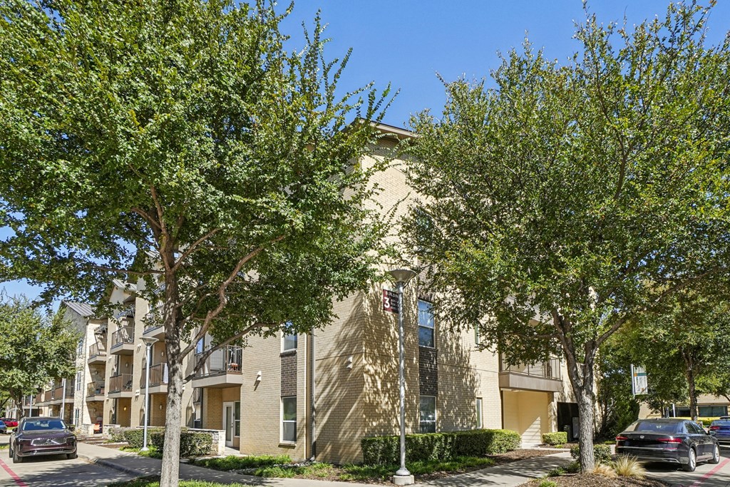 A building with a beige facade is surrounded by green trees.