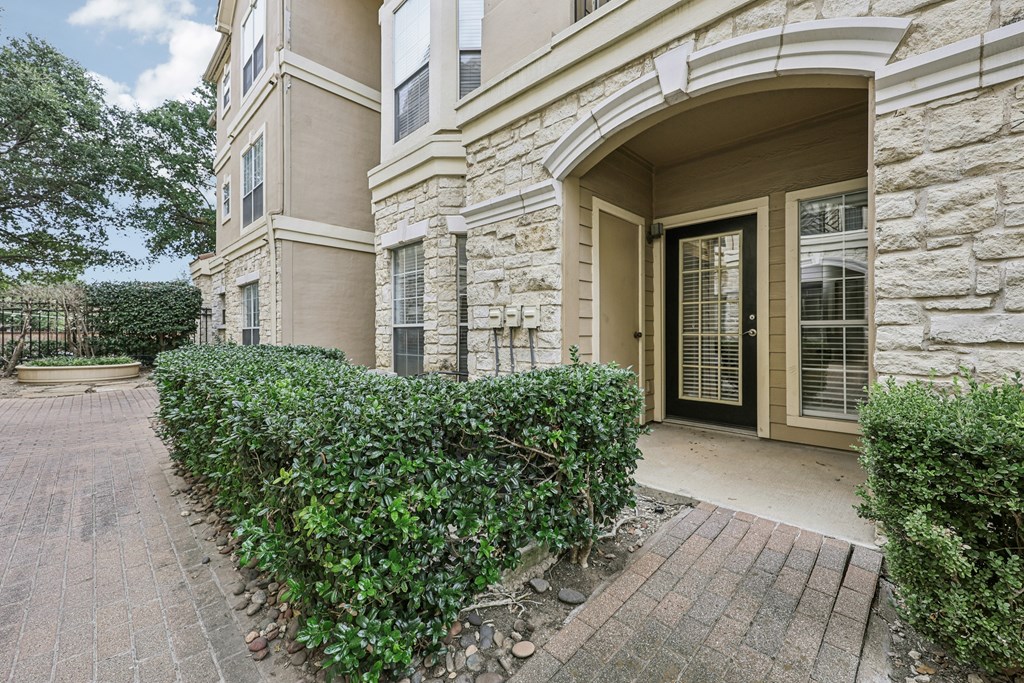 A building with a black door and window is surrounded by green bushes.