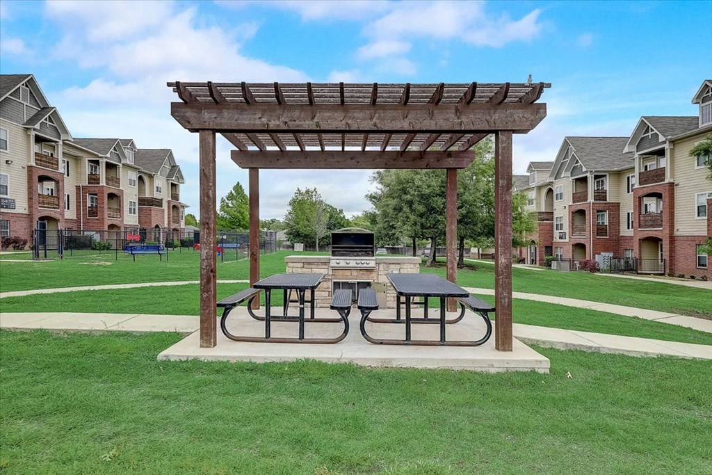 a picnic area with two picnic tables and a fire pit in the middle of a grassy