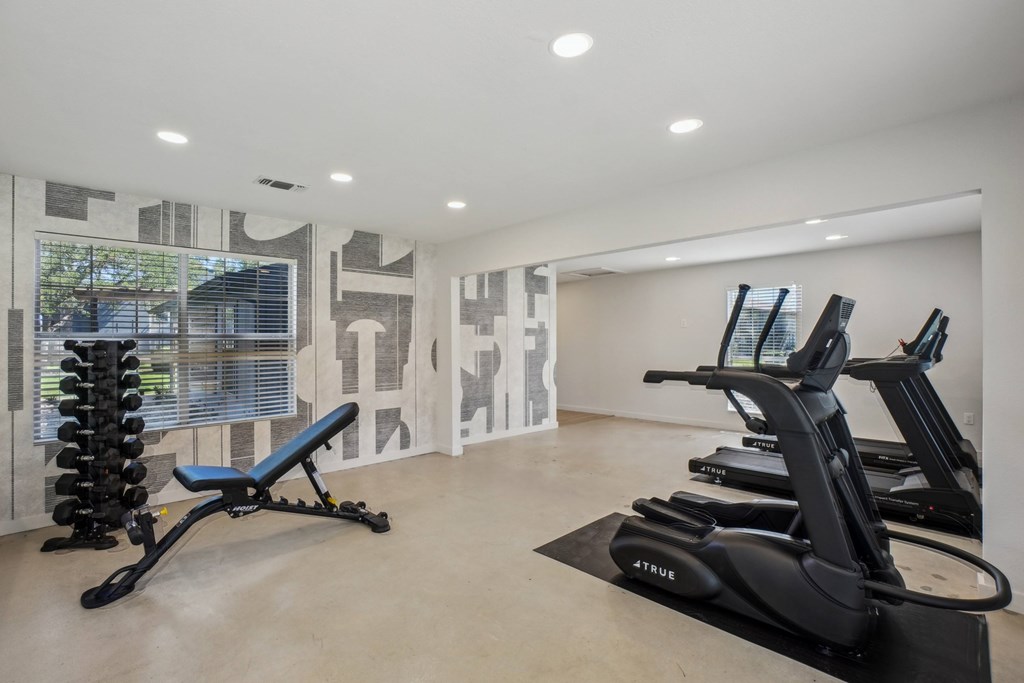 A gym with a row of treadmills and a weight rack.