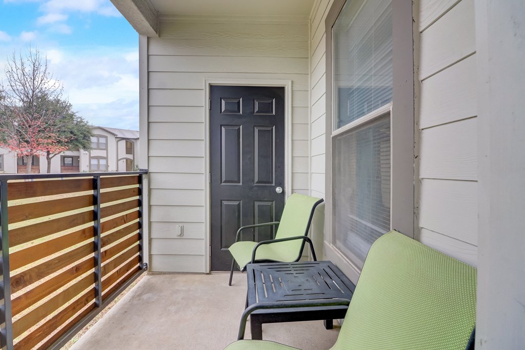 the front porch of a condo with two chairs and a table and a black door