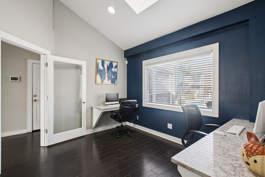 A room with a desk and chairs, a computer, and a window with blinds.
