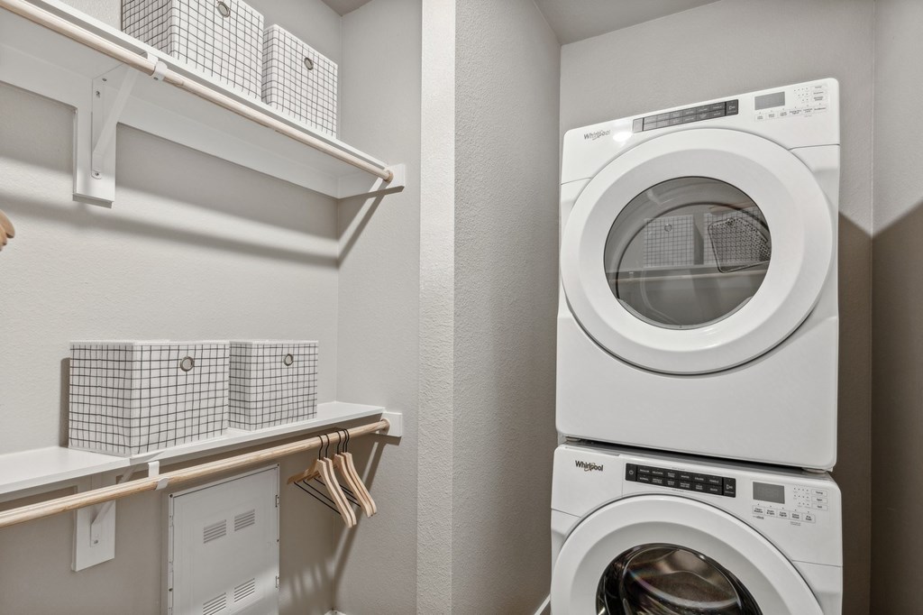A white dryer is stacked on top of a white washer in a small laundry room.