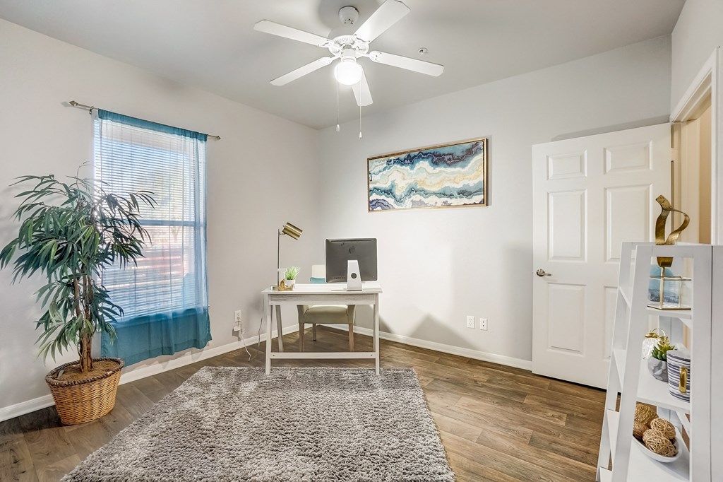 an office with a desk and a ceiling fan and a window