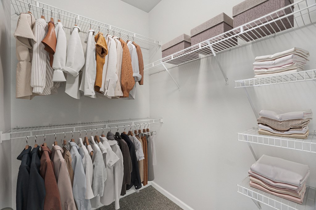 A white closet with clothes hanging and folded towels on shelves.