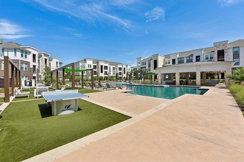 A swimming pool is surrounded by a grassy area and a concrete walkway in a residential area.