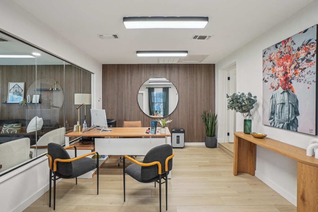A modern office space with a wooden desk, two chairs, and a large mirror on the wall.