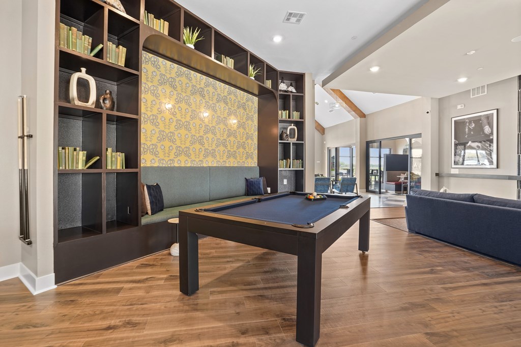 A pool table is in the middle of a room with a bookshelf and a couch.