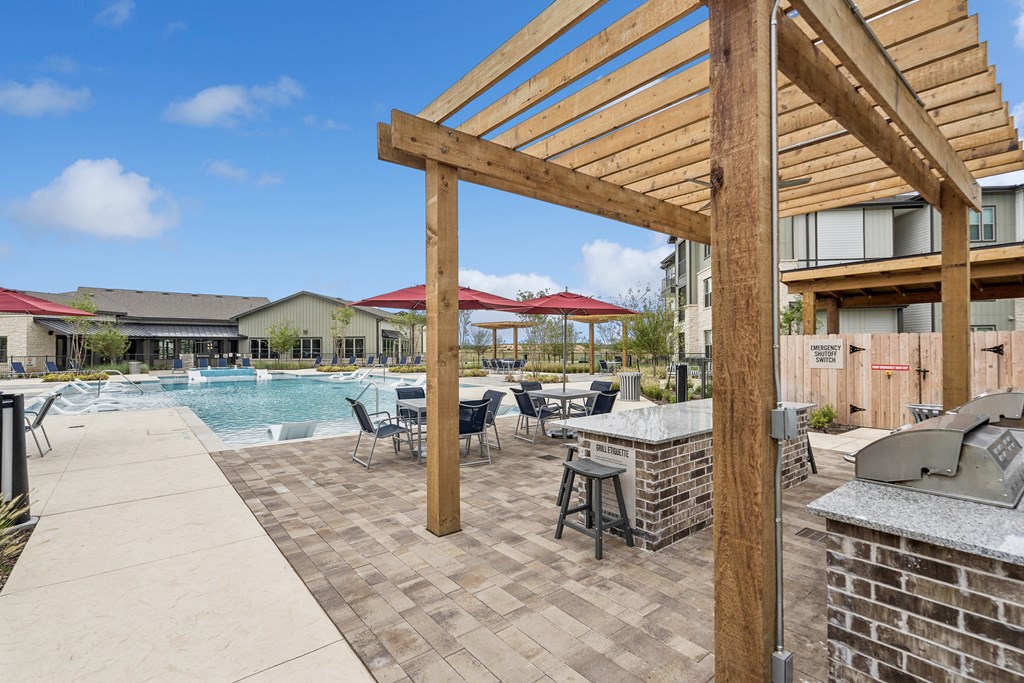 A wooden pergola over a patio with a pool in the background.
