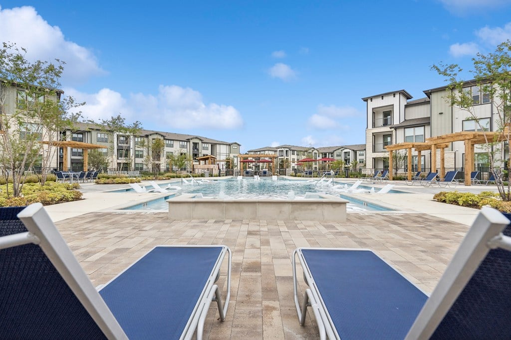 A swimming pool surrounded by a stone patio and lounge chairs.
