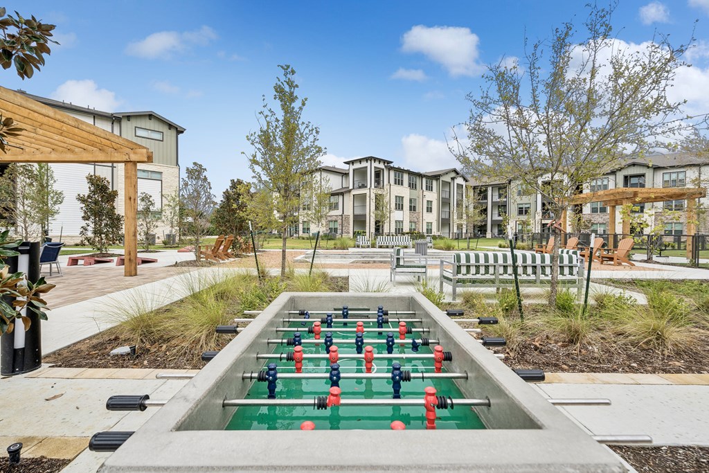 A foosball table sits in the middle of a courtyard with apartment buildings in the background.
