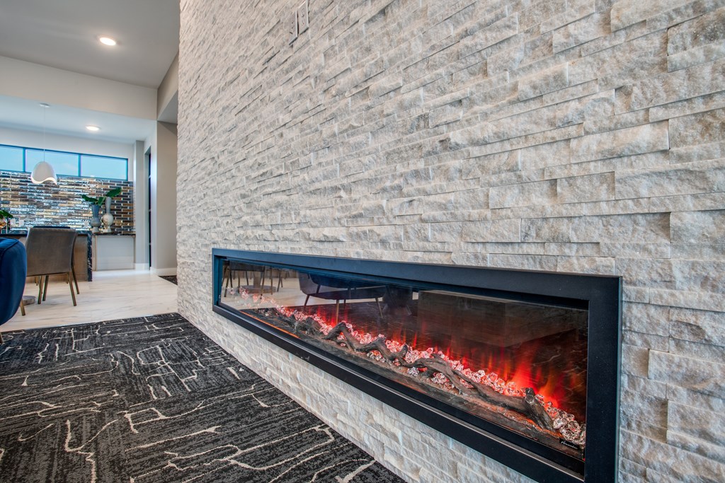 A modern fireplace with a stone wall and a fire burning inside.