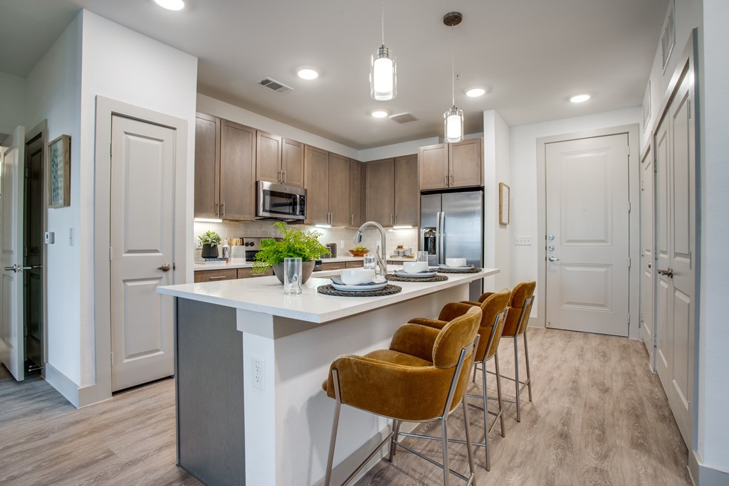 A kitchen with a white island and brown chairs.