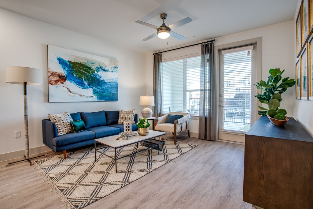 A living room with a blue couch, a painting on the wall, a ceiling fan, and a wooden cabinet.
