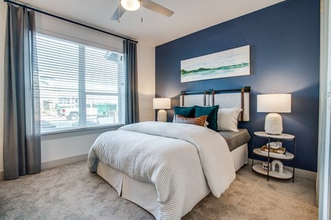 Bedroom with blue accent wall, ceiling fan, and large window for daylight.