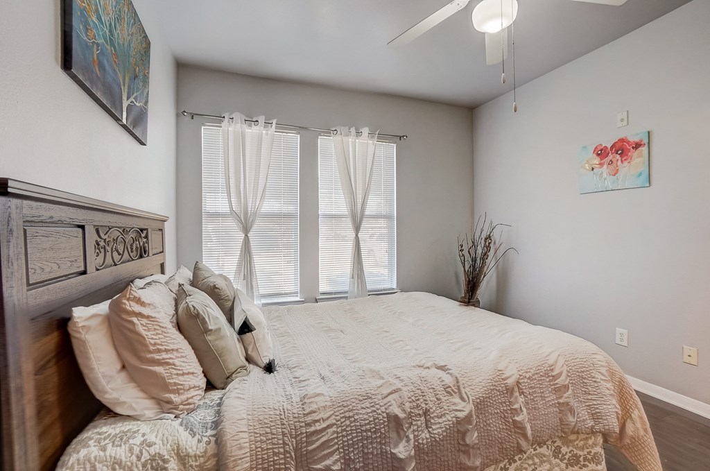 the master bedroom has a large bed and windows with blinds and a ceiling fan