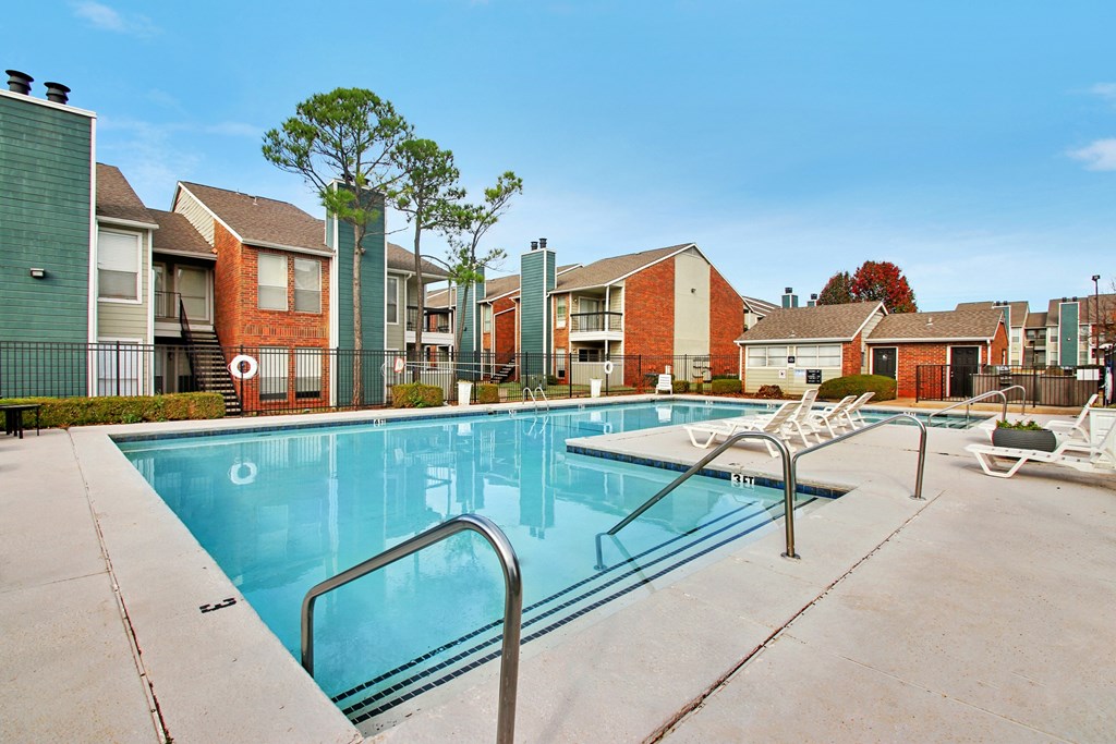 A swimming pool surrounded by a concrete floor and metal railings with apartment buildings in the background.