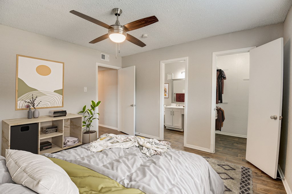 a bedroom with a ceiling fan and a closet with a bathroom in the background