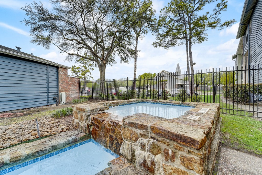 a pool with a stone wall and a fence around it