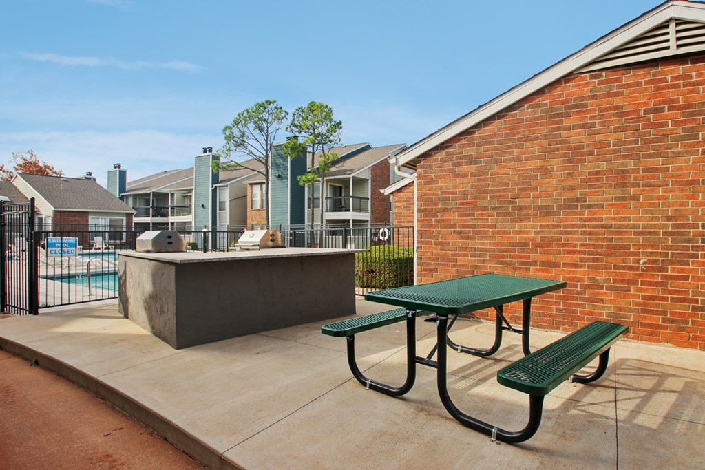 A green picnic table and bench are in front of a brick wall.