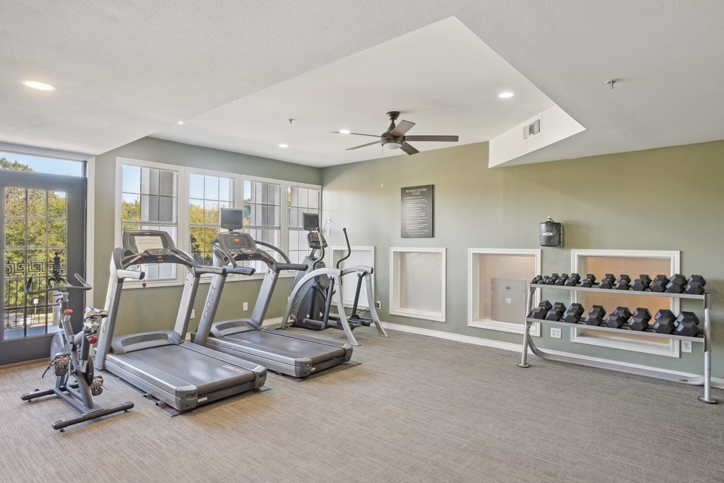 A spacious gym with treadmills, exercise bikes, and a rack of dumbbells.