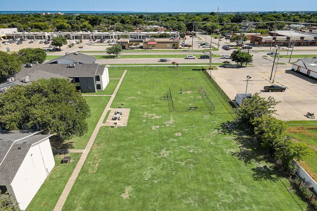 an aerial view of a large grassy field with buildings in the background
