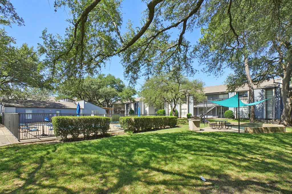 A sunny day at a park with a blue umbrella and a building in the background.