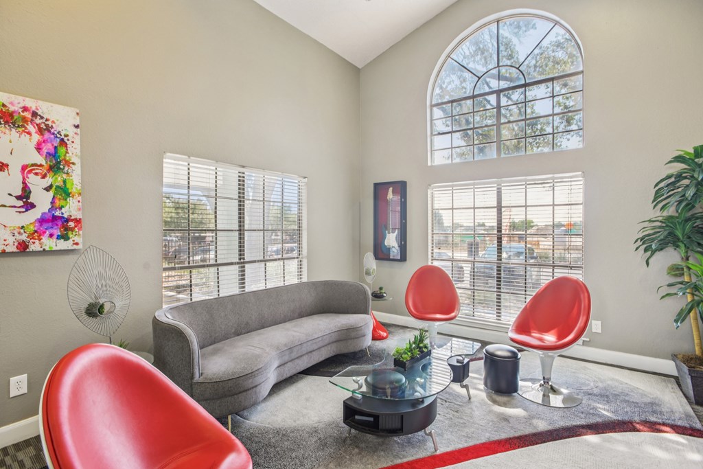 A living room with a grey couch, red chairs, and a fan.