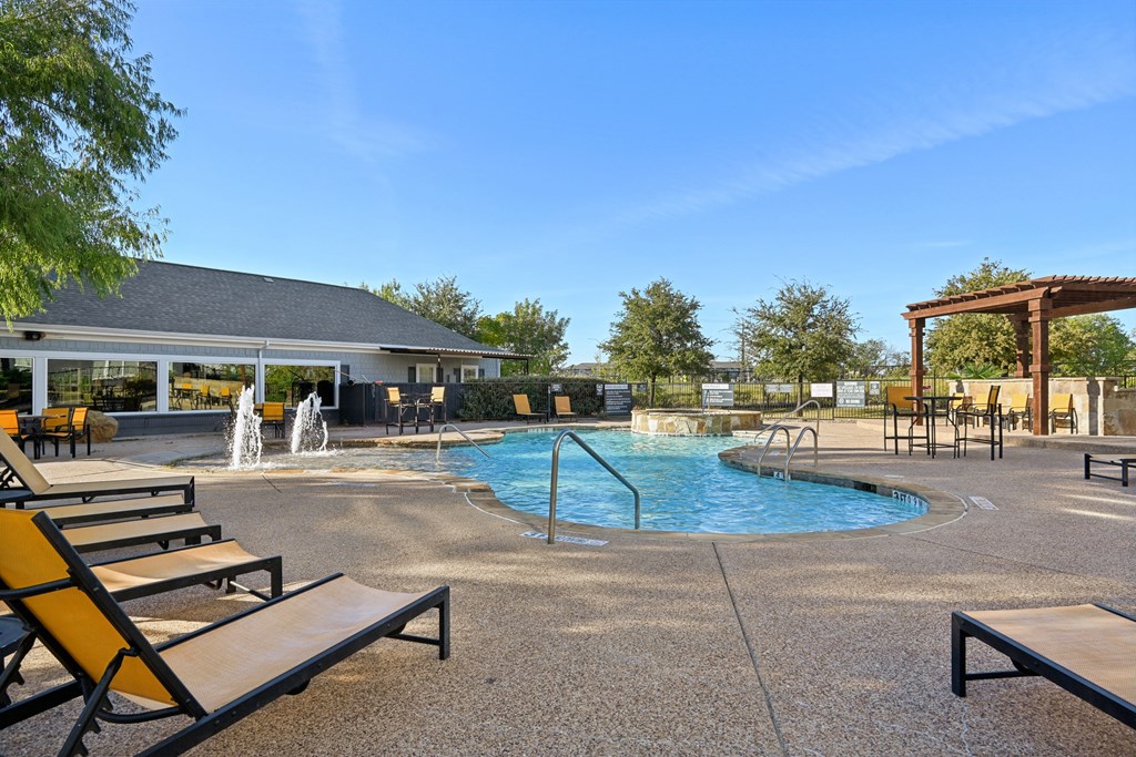 A pool area with a fountain and lounge chairs.