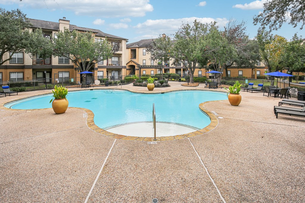 A large swimming pool surrounded by a concrete patio and trees.
